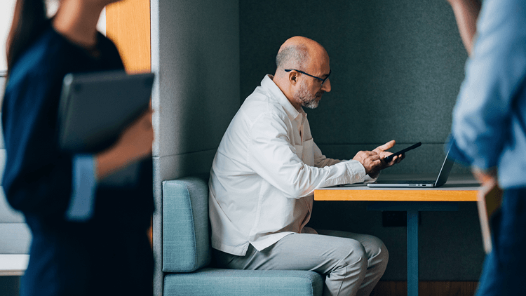 Persoon gebruikt een smartphone aan een werkplek, met collega's op de voorgrond