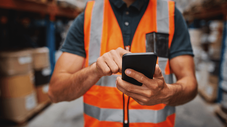 Magazijnmedewerker gebruikt een smartphone in een magazijn.