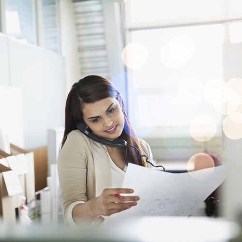woman on the phone looking at a plan on paper