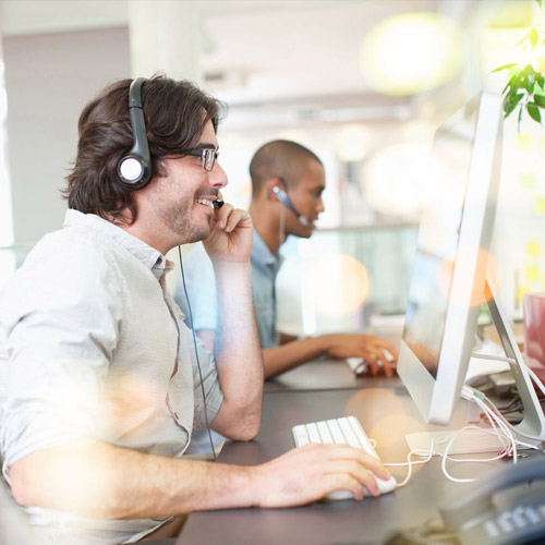 Group of operators at work. Call center. Focus on young man receptionist in headset at customer service. Business concept and casual clothing style