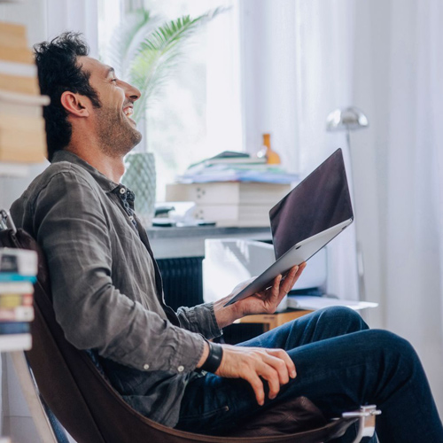 man laughing on a chair with a laptop in his hand