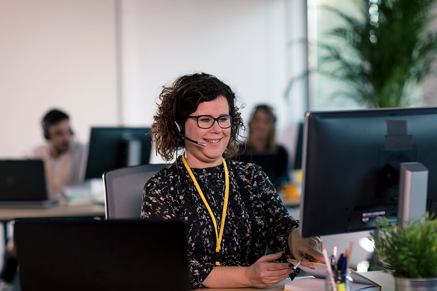 woman with headset in front of her computer smiling in the office