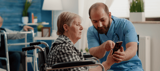 Man in scrubs toont bewoner in rolstoel iets op mobiele telefoon