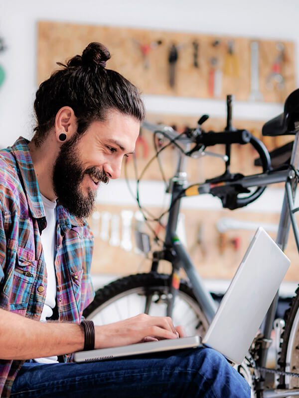 A man with a beard sitting down in a bike store with a laptop on his lap