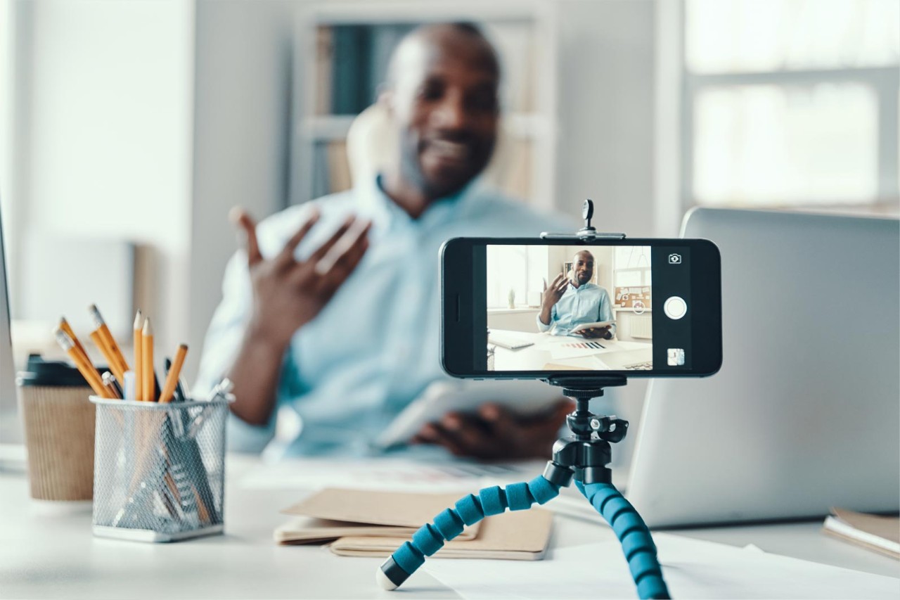 Handsome young African man in shirt telling something and smiling while making social media video