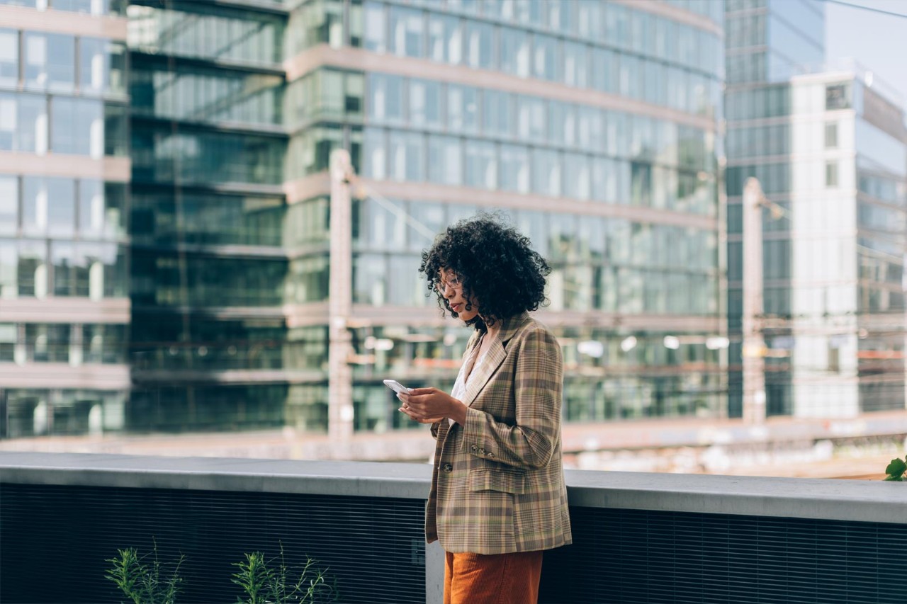 fashion brazilian woman using mobile phone - trendy business working woman under skyscrapers looking at smartphone
