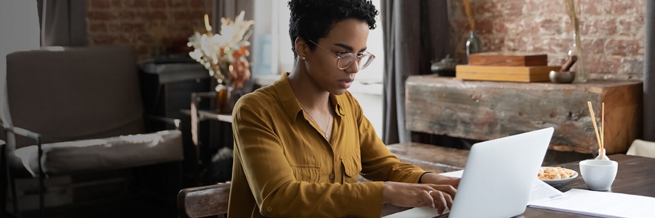 A woman in a yellow blouse is typing on a laptop