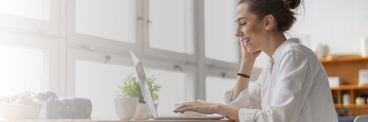 Woman sitting at the table smiling in front of a laptop