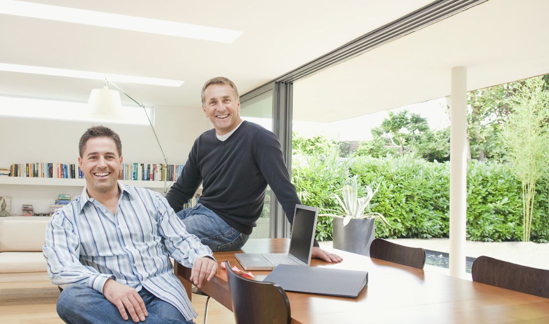 two men laughing at table with laptop in front