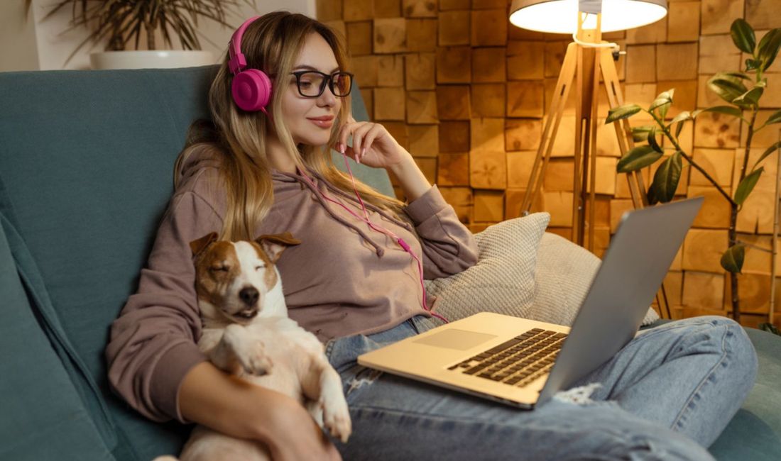 woman and dog in sofa with laptop and headphone